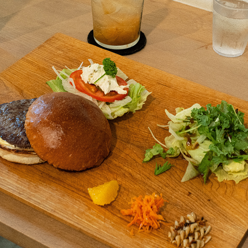 木のプレートにのったハンバーガーとサラダとショートパスタとフルーツ